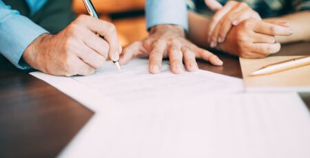 Close-up of a person's hands signing a document form on a table.